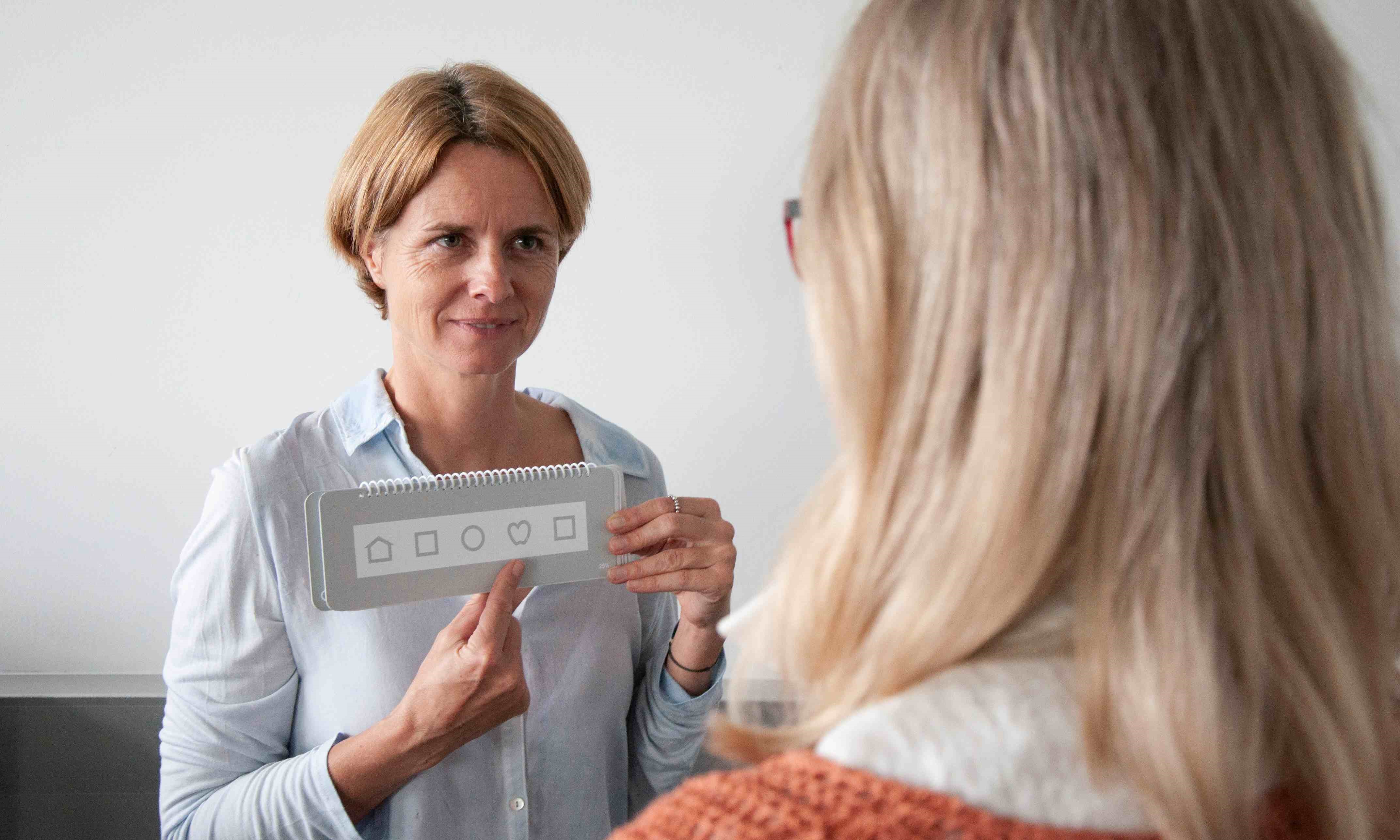 Orthoptistin zeigt einer Frau eine Sehzeichentafel