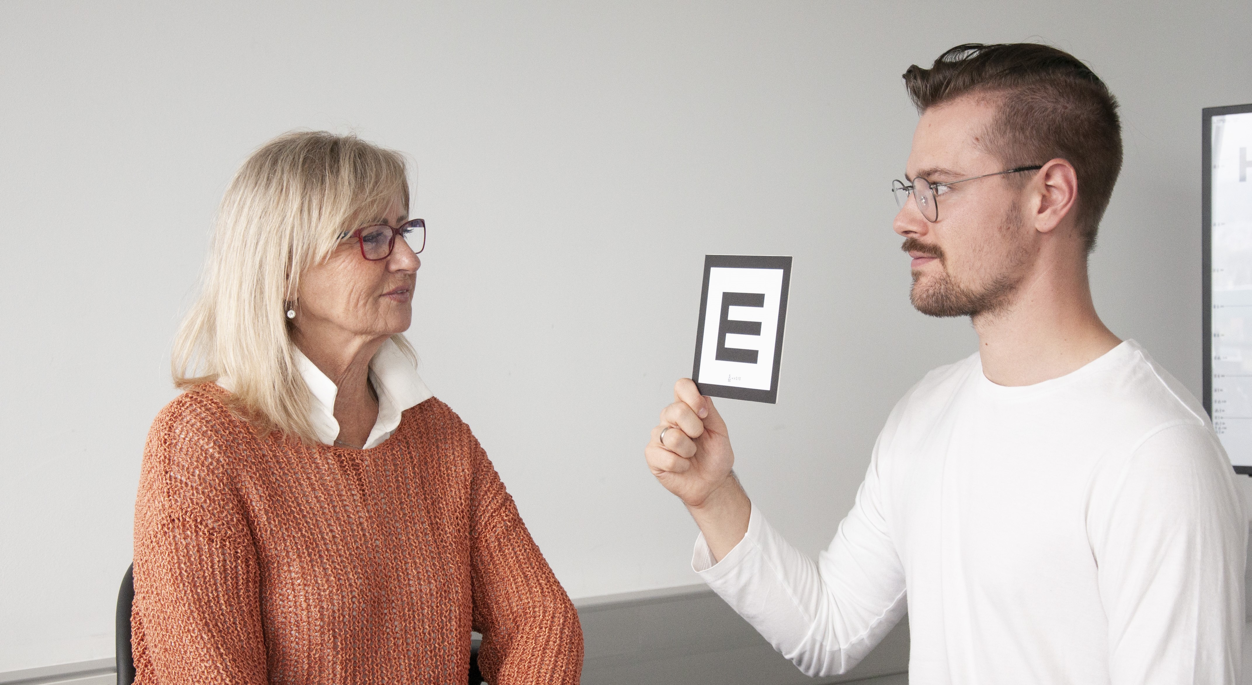 Mann zeigt einer Frau eine Sehzeichenkarte