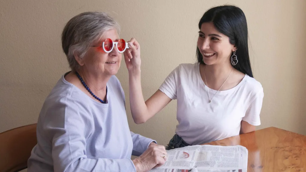 Orthoptistin hält einer älteren Dame ein Brillenglas zum Testen vor