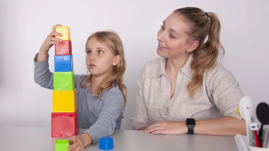 Kind baut mit Orthoptistin einen Becherturm