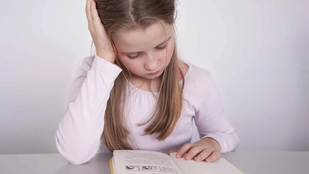 Mädchen liest ein Buch und hält sich den Kopf